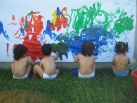 bimbi seduti di spalle che disegnano con le tempere su un muro